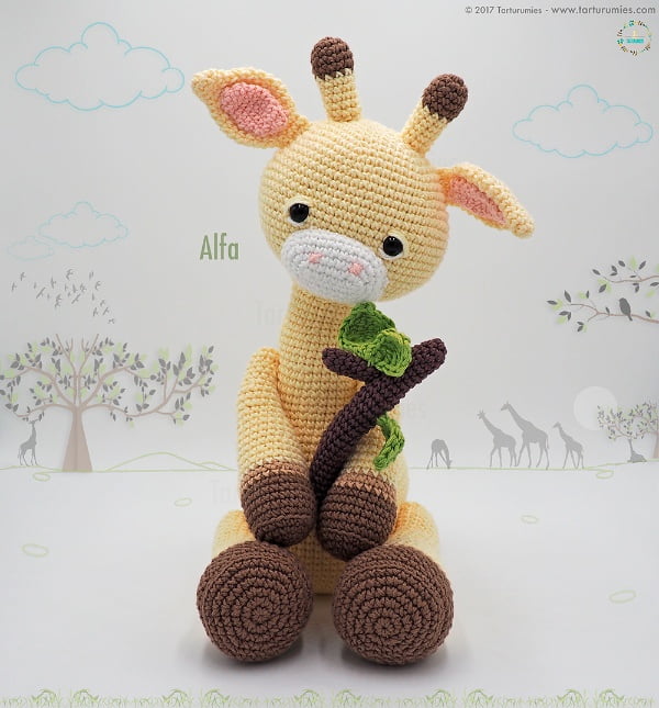 Amigurumi crochet giraffe holding a branch.