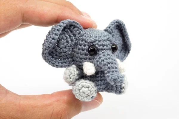 Tiny crocheted elephant amigurumi with tusks and big ears.