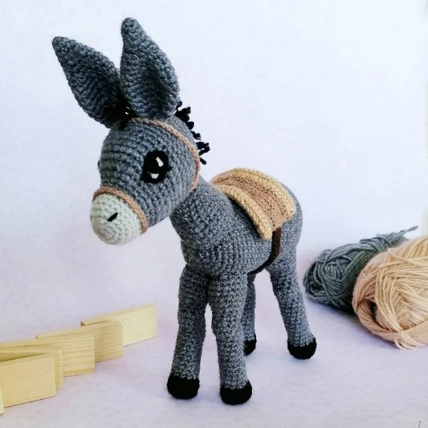 Standing amigurumi crochet donkey with saddle.