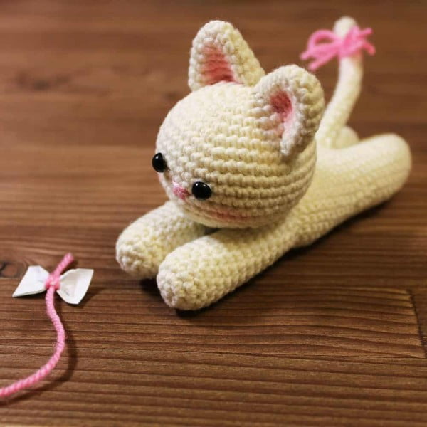 White amigurumi kttten playing with pink string.