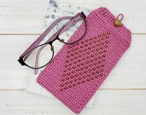 Pink beaded eyeglass case and glasses on a white timber backgorund..