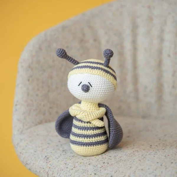 Pale lemon and gray amigurumi bee with crossed arms.