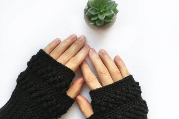 Person wearing black crocheted fingerless mittens.