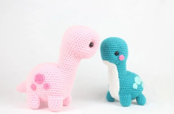 A pink and a blue crochet Brontosaursus dinosaur.