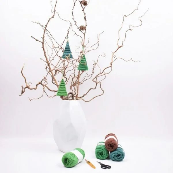 Crochet Christmas trees hanging from a twig tree in a vase.