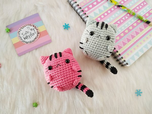 Two chubby amigurumi cats, one bright pink and one gray.
