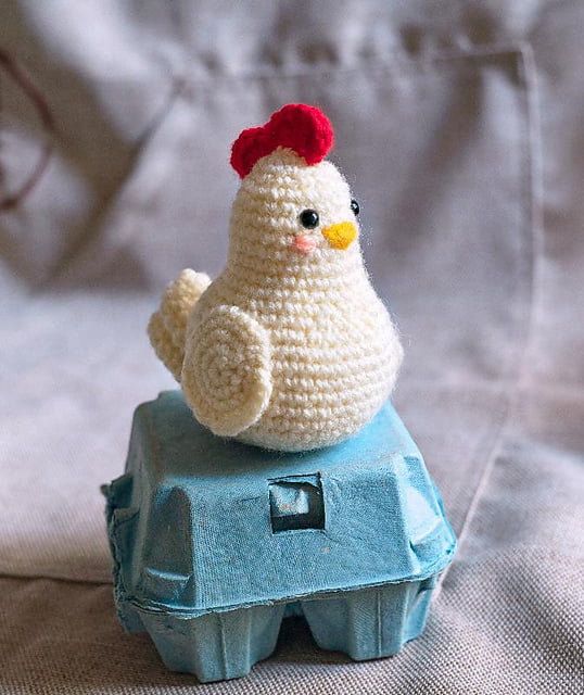 Crochet hen sitting on an egg carton.
