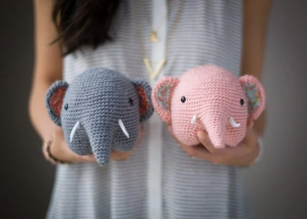 Two chubby crochet elephants, one gray and one pink.