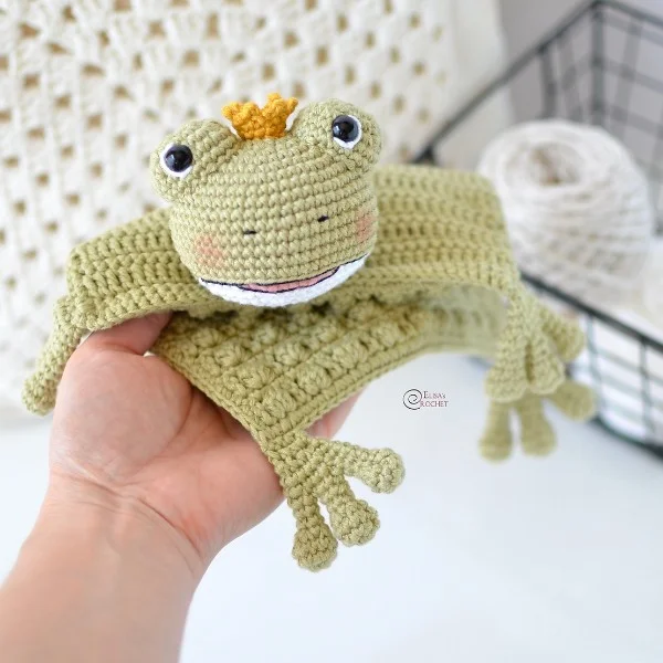 Green crochet frog baby lovey with a little golden crown.
