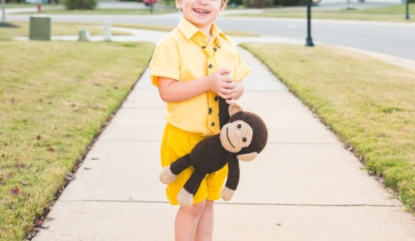 Little boy dressed as Curious George holding a crochet monkey toy.