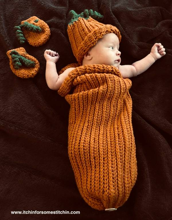 A young baby in a crochet pumpkin themed sleep sack.
