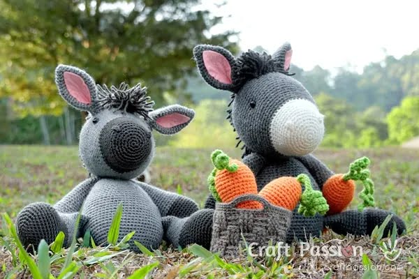 Two crochet donkeys in a field with crochet carrots in a basket.
