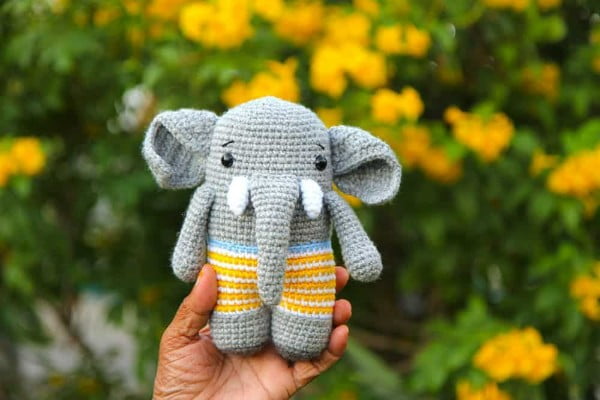 Amigurumi elephant with tusks wearing strped shorts.