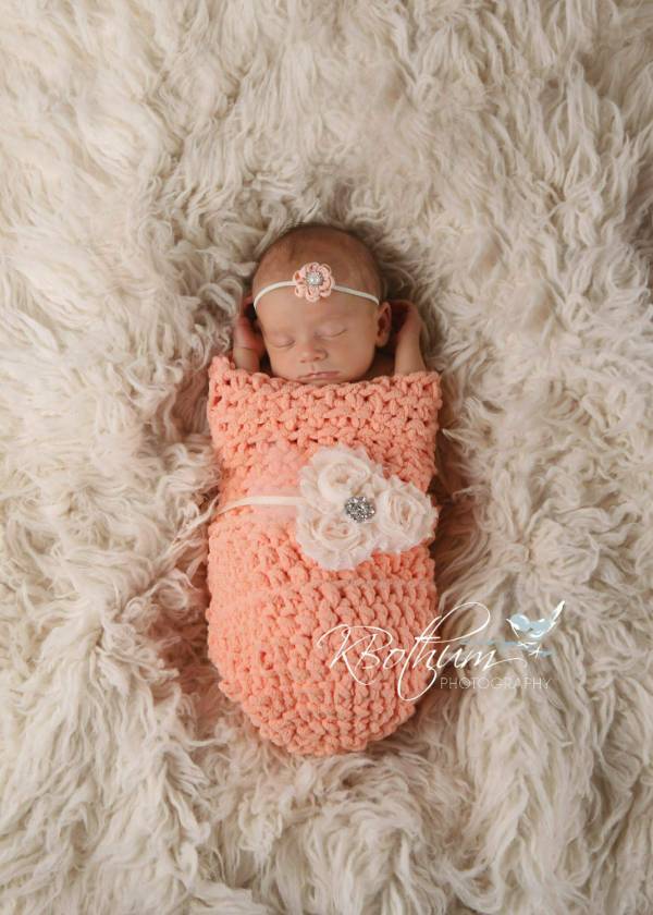 A little baby asleep in a peach colored crochet baby cocoon.
