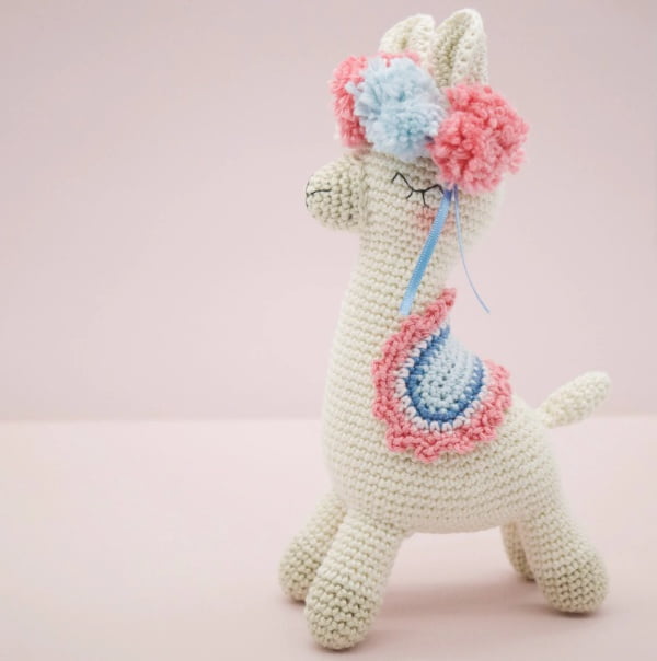 Crochet llama with pom poms and frilly pink saddle blanket.