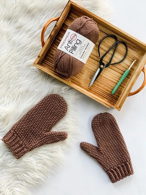 A pair of knit-look crochet mittens and a tray holding crochet materials.