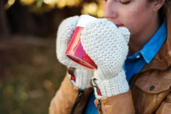 Woman wearing crochet mittens while drinking a hot beverage.