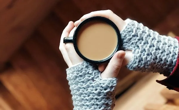 Person holding a cup of coffee and wearing gray crochet mitts.