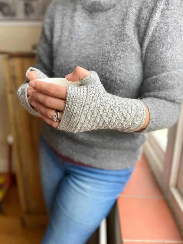 Person wearing crochet mitts holding a hot drink.