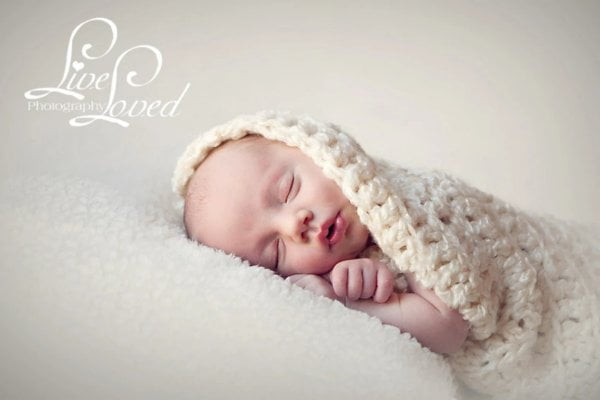 Newborn baby sleeping in chunky white crochet baby cocoon.