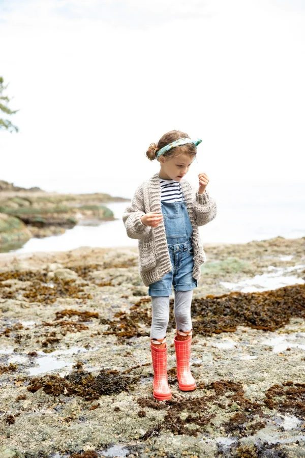 Young girl at the beach wearing an oversized crochet cardigan.