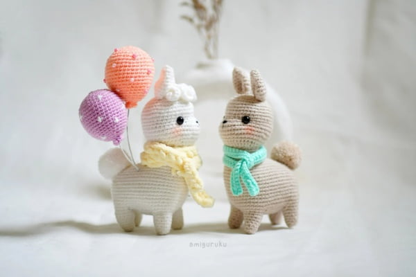Two little crochet amigurumi alpaca with scarves and crochet balloons.