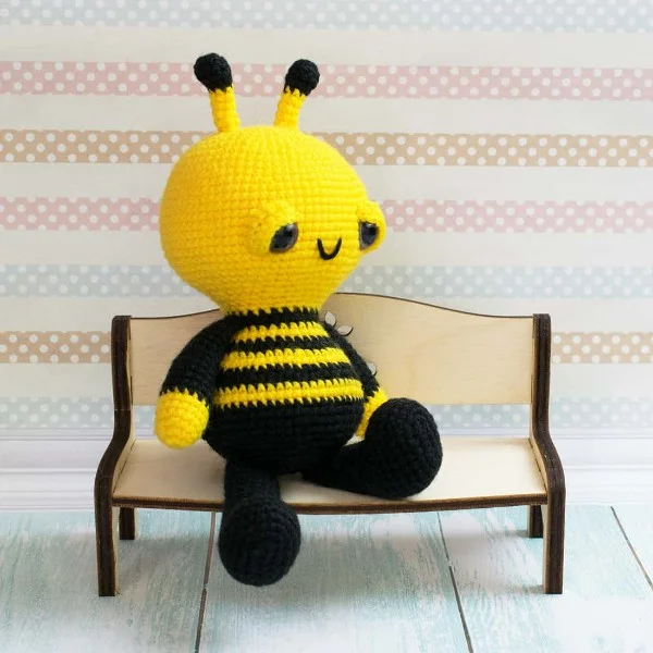 Amigurumi bee with sleepy eyes sitting on a bench.