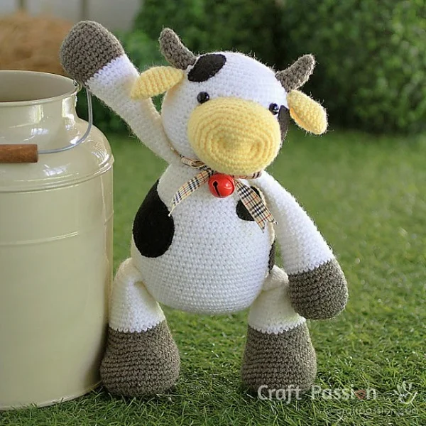 Crochet cow plushie standing next to a milk can.
