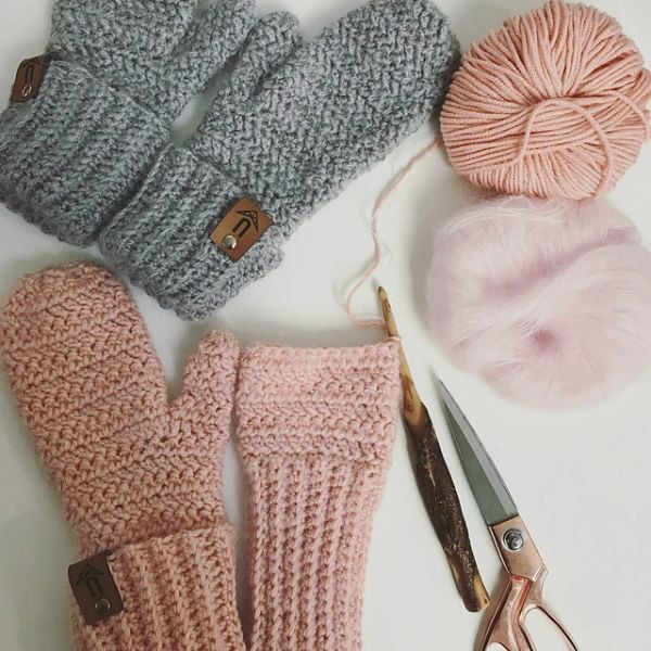 Two pairs of crocheted mittens, one pink and one gray.
