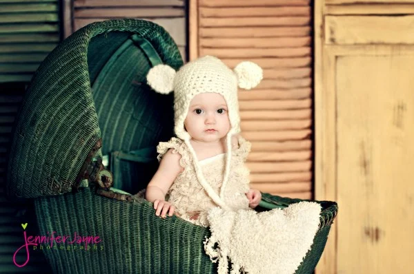 Baby in a pram wearing a crochet bear hat.