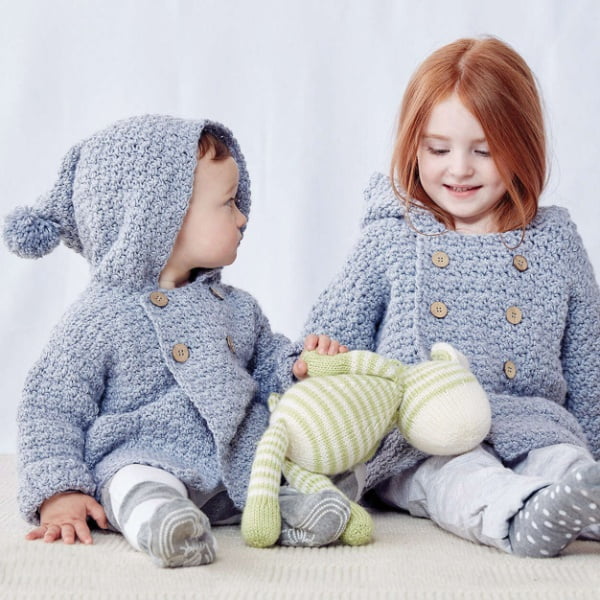 A baby and a young child wearing hooded crochet jackets