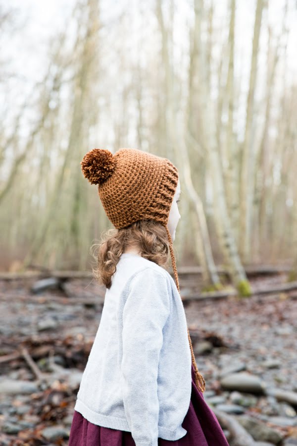 A young child wearing a crochet bonnet beanie with a pom-pom on top.