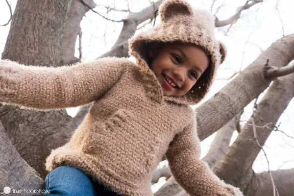 Little girl in a tree wearing a crochet baby bear hoodie