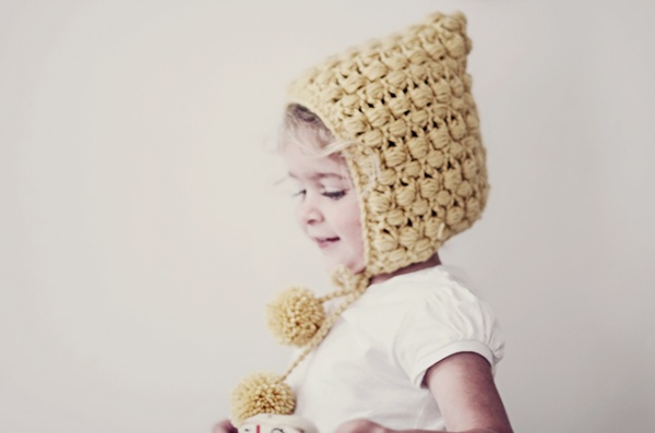 Little girl wearing pixie-style crochet bonnet with pompom detail.