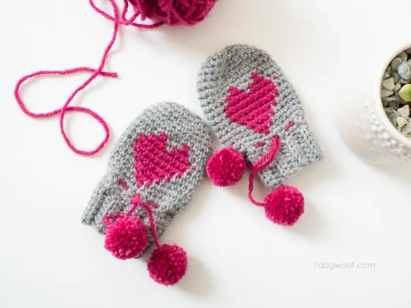 Crochet baby mittens with heart motif and pompoms.