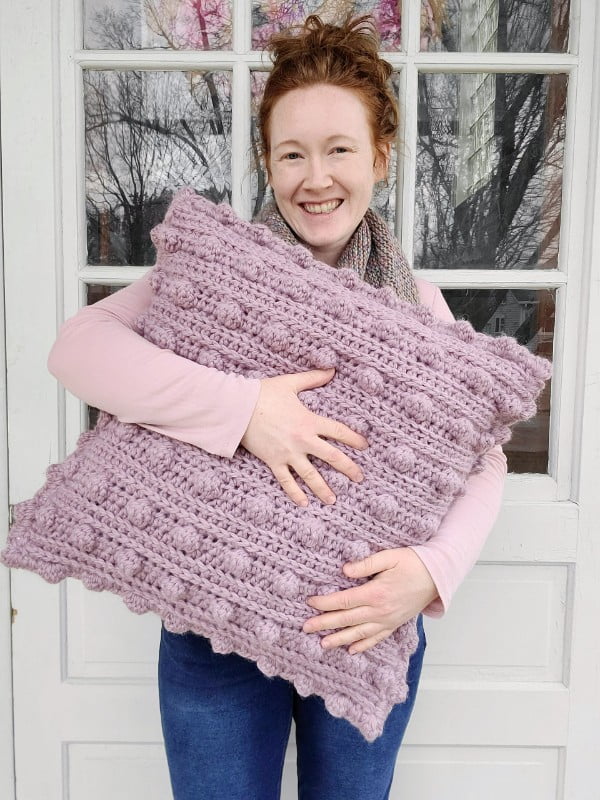 Woman holding a large pink crochet pillow.