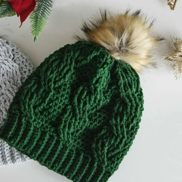 A green cable crochet beanie with a faux fur pompom.