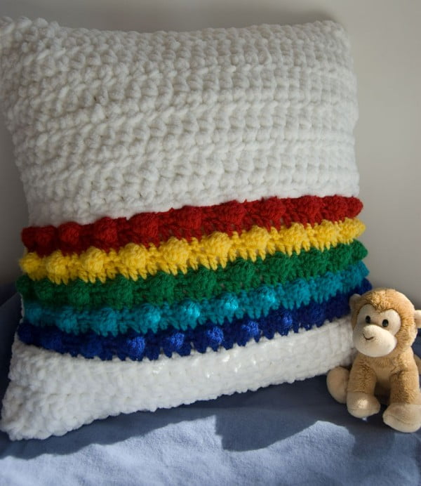 White crochet pillow with rainbow stripes.