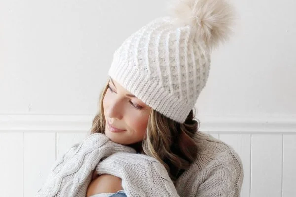 A woman wearing a white crochet beanie with a large pompom.