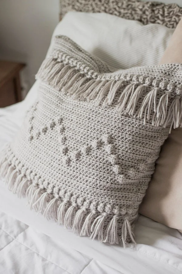 Grey crochet pillow with fringing.