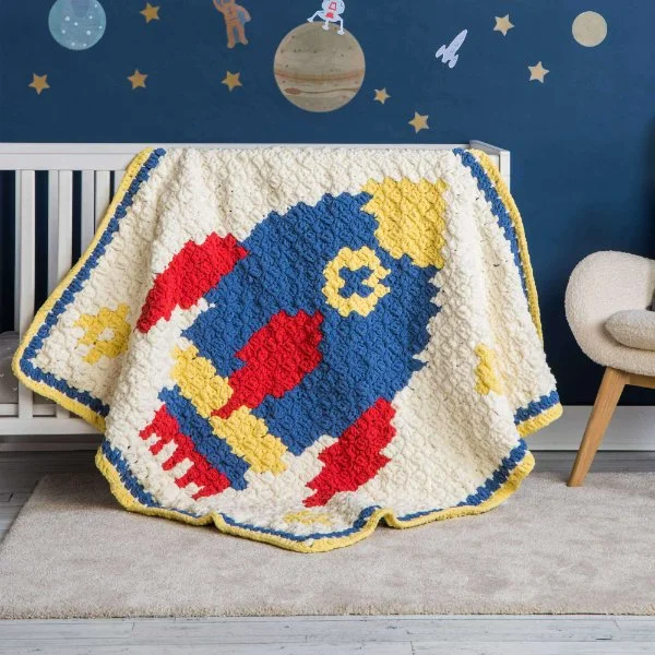 A C2C crochet rocket ship blanket draped over a cot in a space-themed nursery.