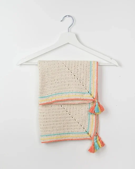 A crochet baby blanket hanging on a wooden clothes hanger.