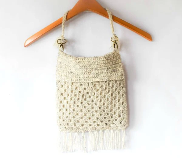 Granny square crochet bag with fringing hanging from a wooden coat hanger.