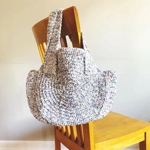 A crochet bag hanging off the back of a wooden chair.