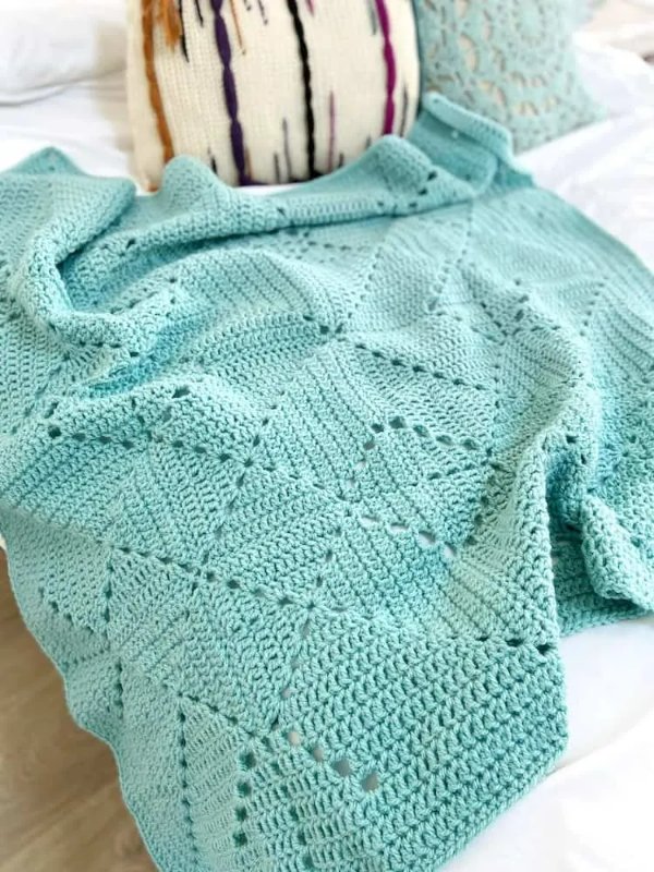 A simple blue crochet blanket on a bed.