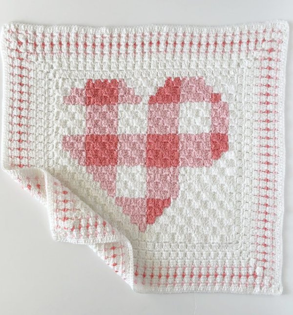 A pink and white gingham C2C crochet baby blanket with a large heart motif.
