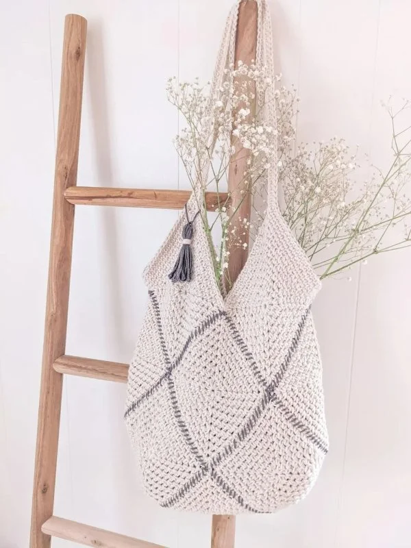 Grey and white granny square bag with flowers hanging off timber ladder.