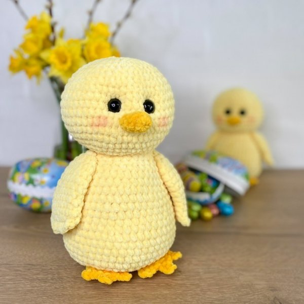 A soft crochet baby chick toy in front of some easter eggs.