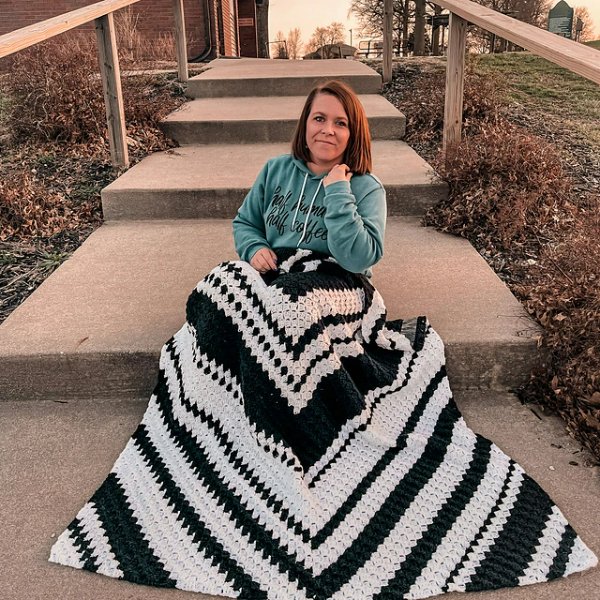 A woman sitting on steps with a black and white c2c crochet blanket on her lap.