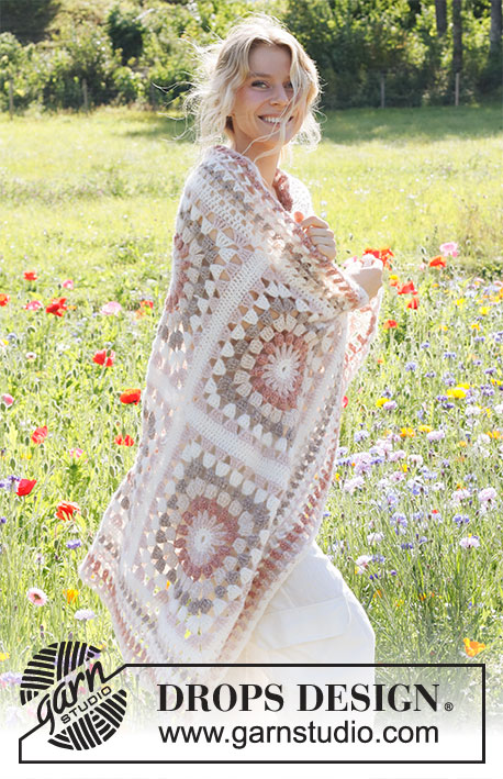 A woman wrapped in a muted colour granny square blanket.